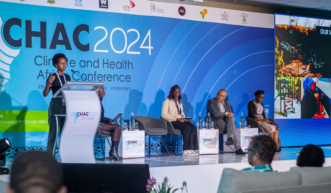A speaker presents at a podium during a CHAC 2024 Climate and Health Africa Conference panel, with four panellists seated on stage and audience members watching.