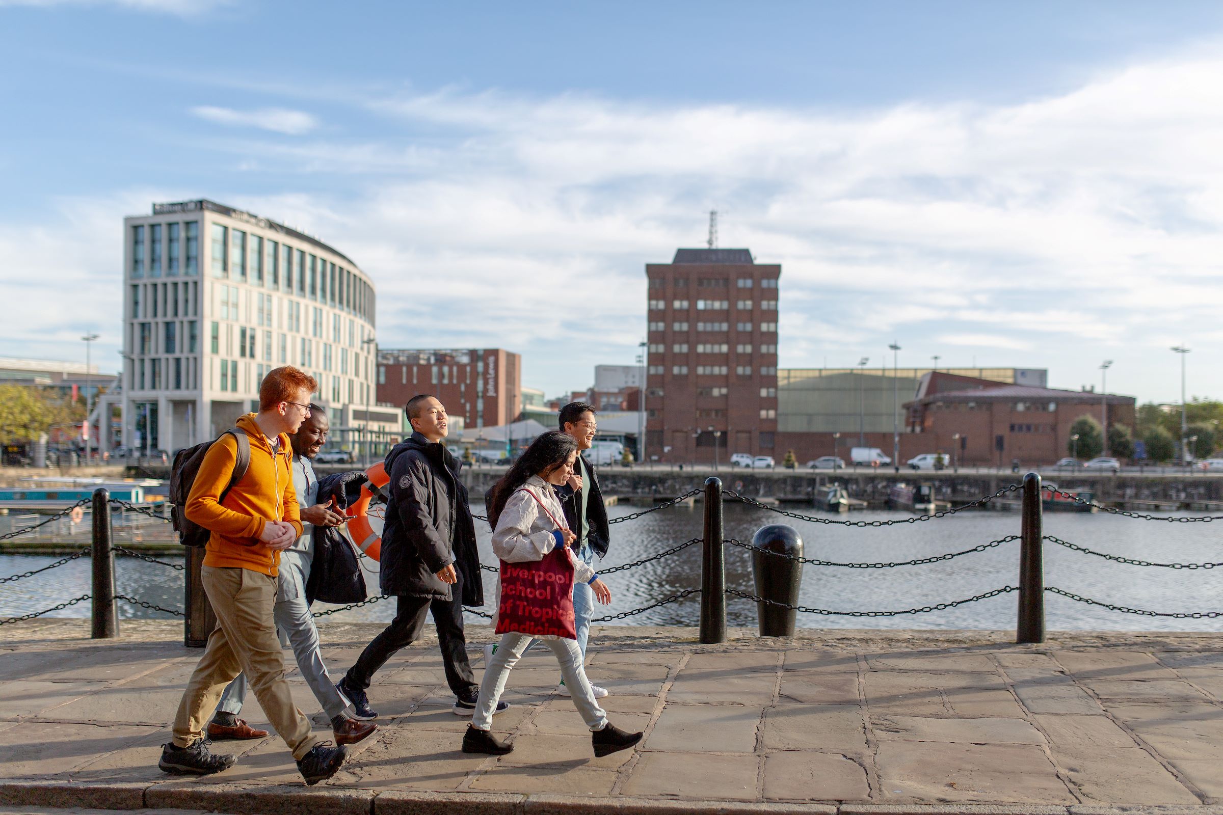 This is a photo of a group of students walking along the Liverpool Docks on a sunny day.