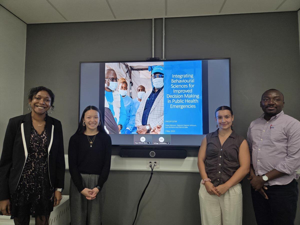 The group of 4 LSTM students stand in front of a TV screen presenting their work