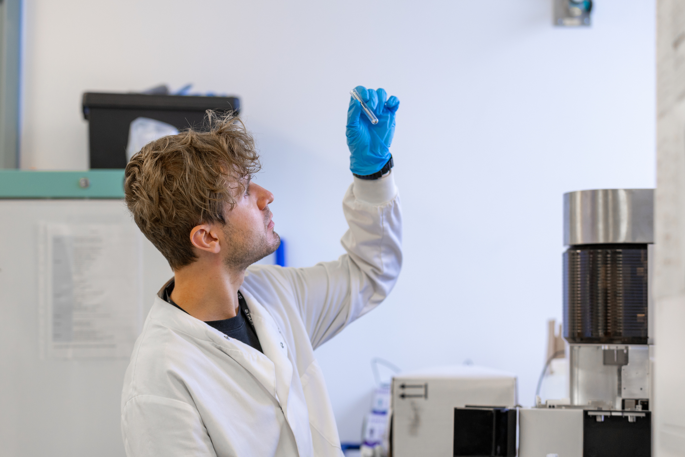 Photo of a male researcher in a lab holding up a test-tube