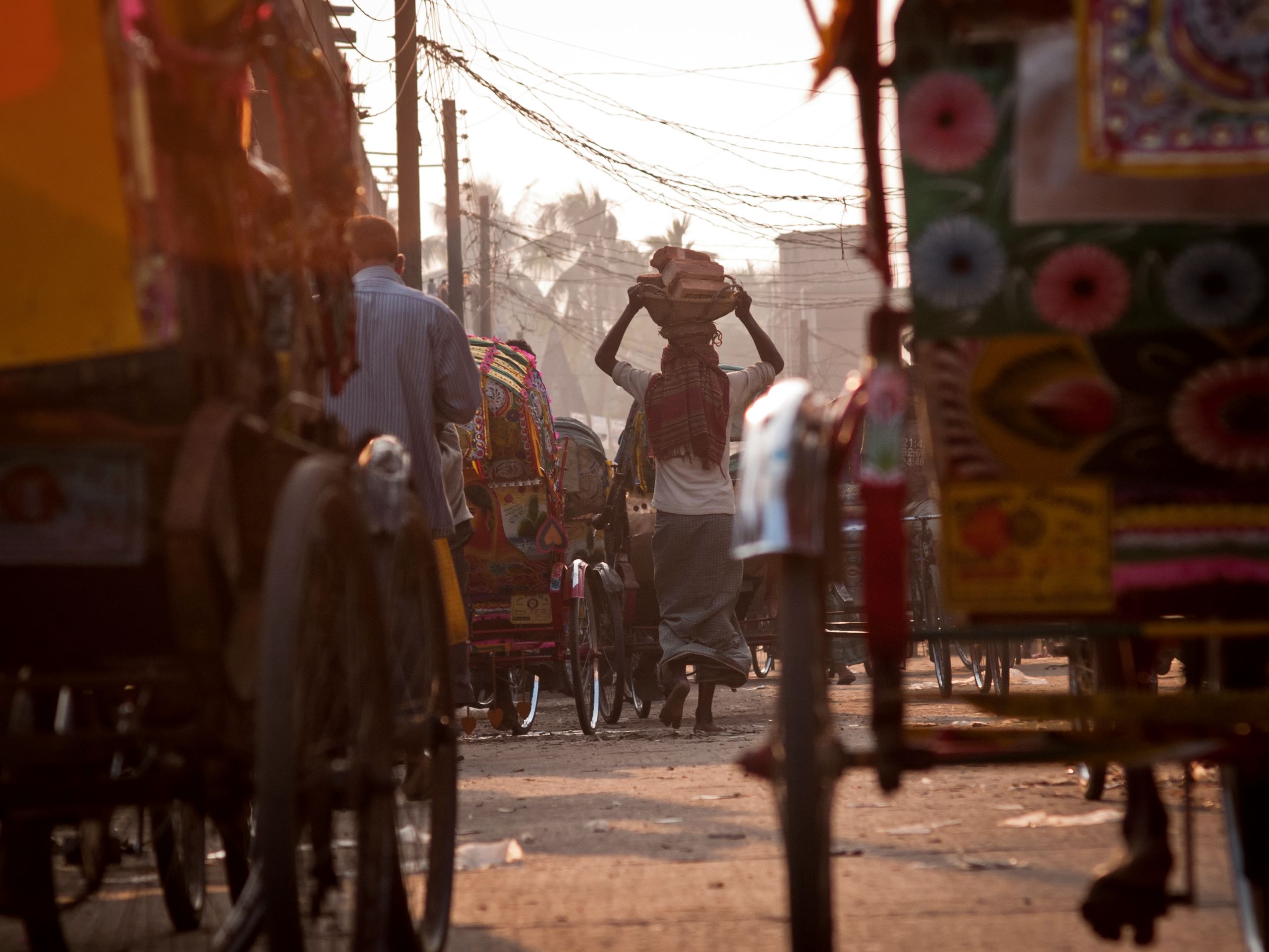 Dhaka, Bangladesh - February 2, 2012: A man carrying a basket full of bricks on his head while he passes through the crowd on the street full of rickshaws.