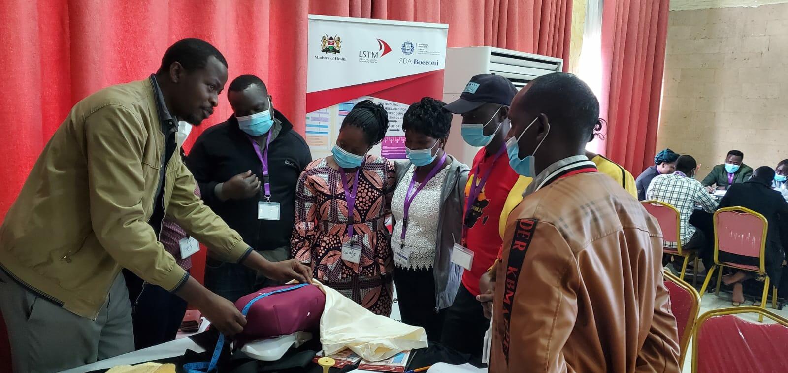 A group of students stood around a training dummy while a lecturer speaks to them and demostrates with a tape measure.