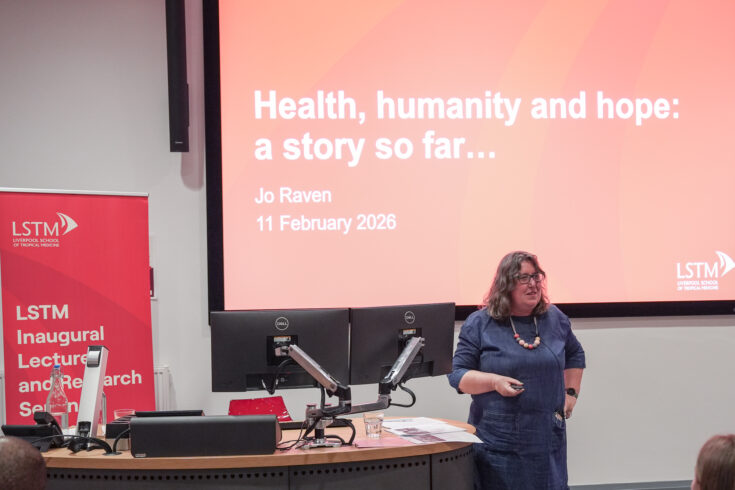 Speaker at an LSTM Inaugural Lecture and Research Seminar stands beside a projection screen showing the slide title “Health, humanity and hope: a story so far…” with the name Jo Raven and the date 11 February 2026.