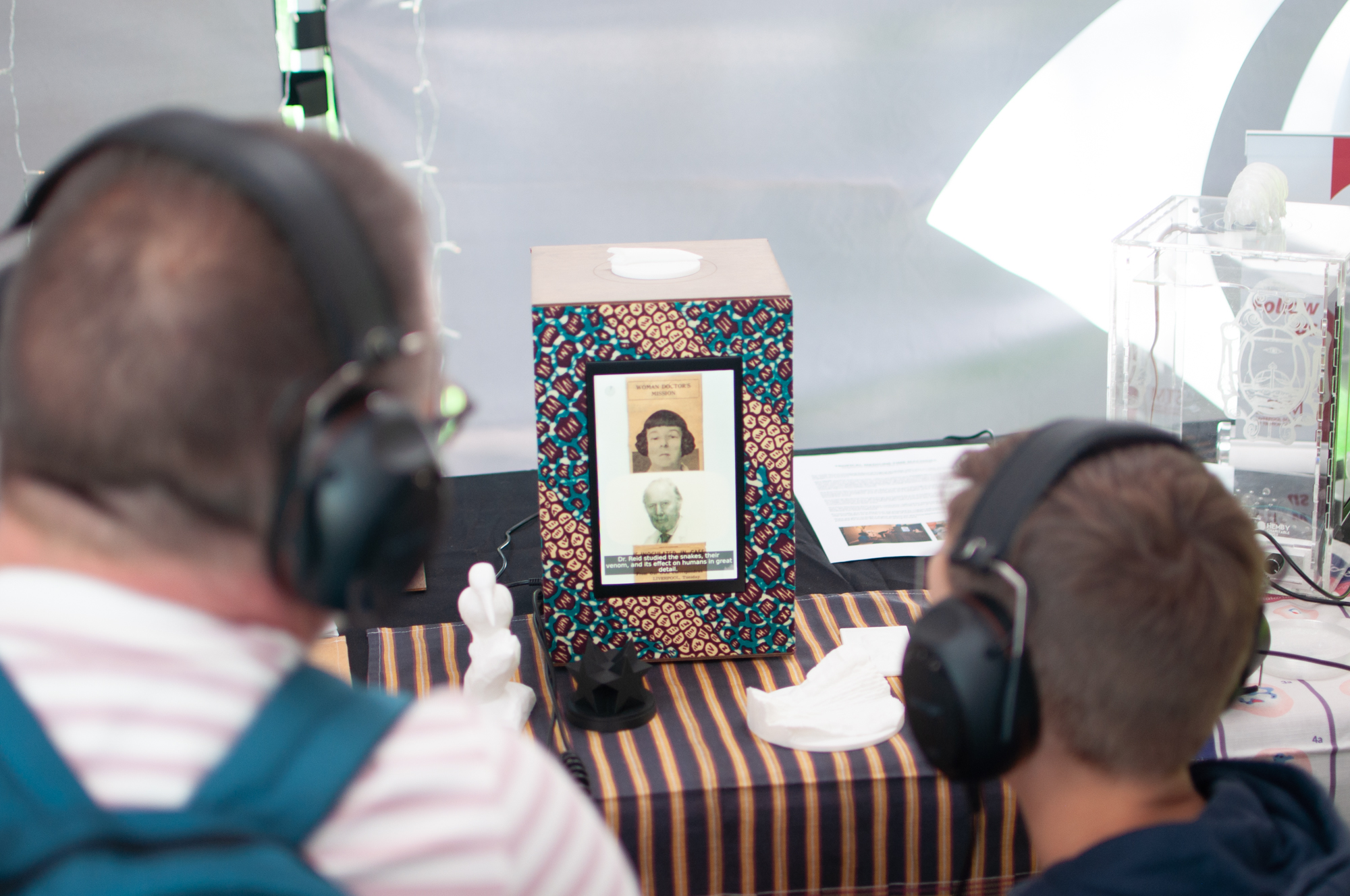 Photo of two people wearing headphones looking at and LSTM time machine box.