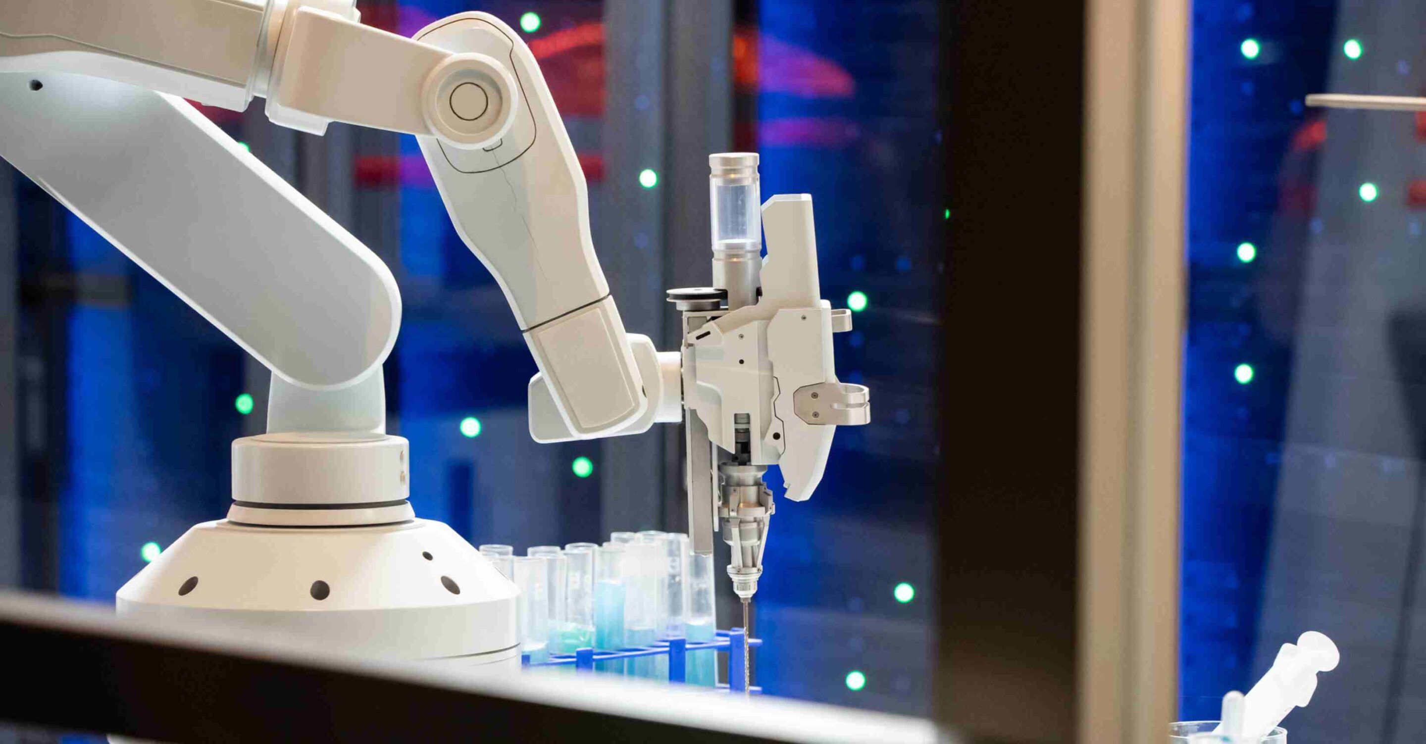 Two white robotic arms in a laboratory setting use syringe-like tools to transfer pink liquid between a small vial and a larger bottle on an automated workstation.