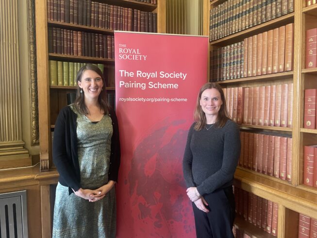 Two women stand in front of a pull-up banner that says Royal Society Pairing Scheme