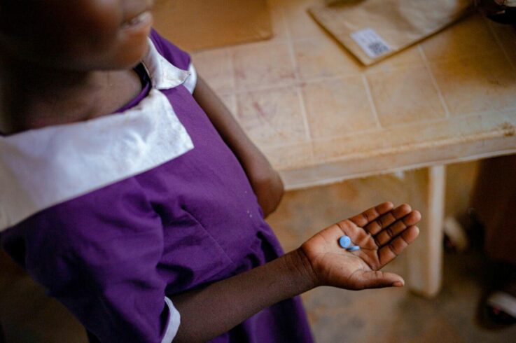 Student in a school uniform holds malaria prevention tablets during a school-based health program.